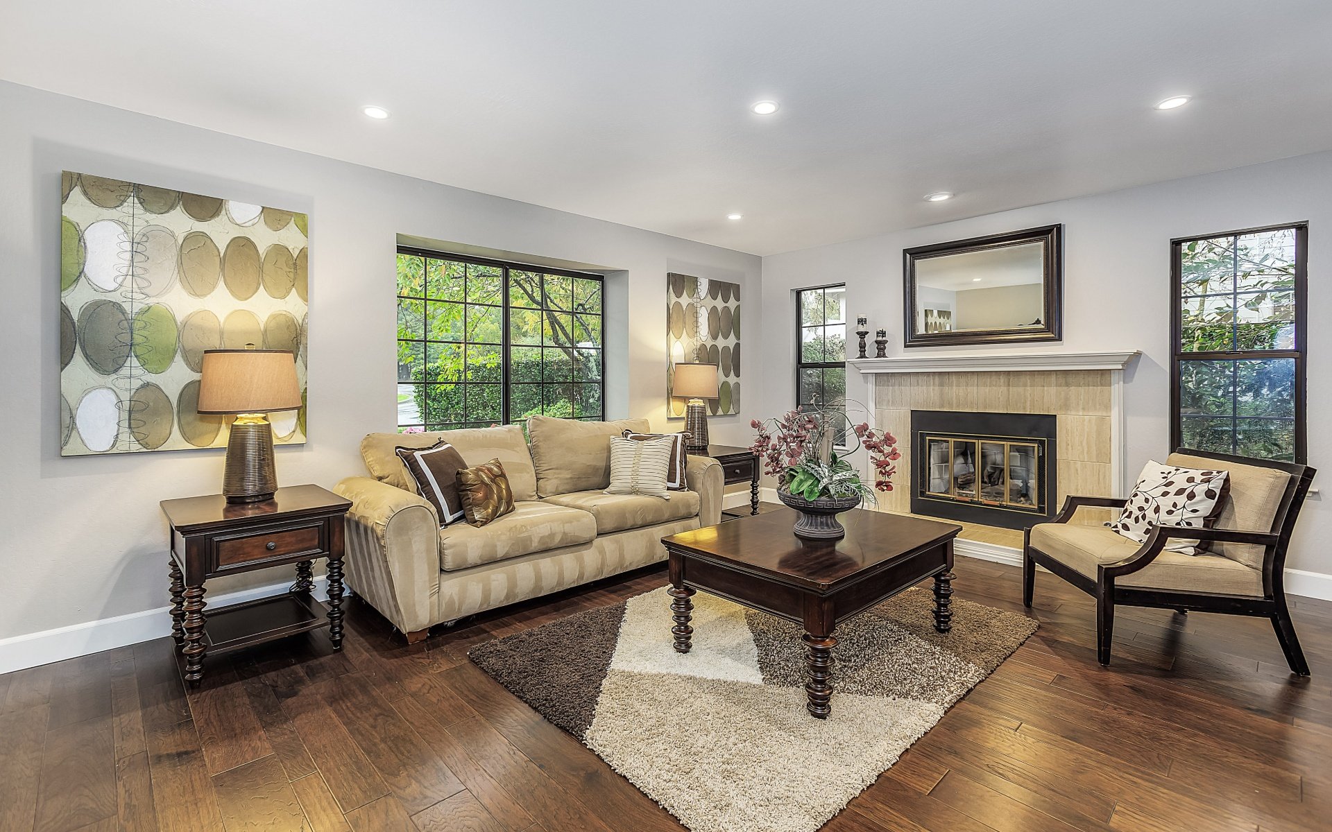Living room with a tiled fireplace, beige seating, dark wood floors, and large black-grid windows.