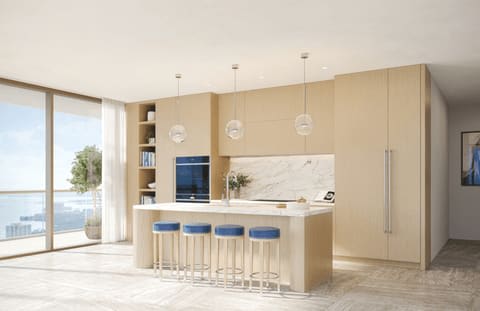 Modern condo kitchen with a marble island, blue bar stools, and water views through floor-to-ceiling windows.