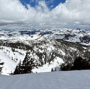 Snow-covered mountain ranges and forested slopes beneath a cloudy sky.
