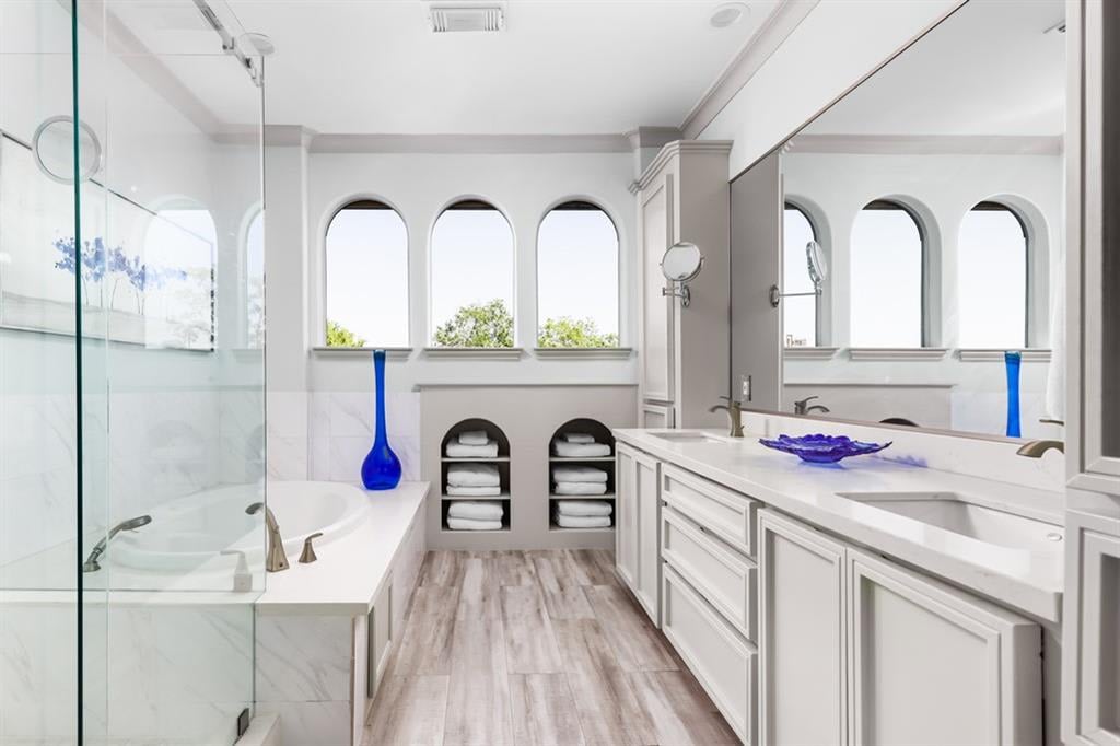 Bathroom with a glass-enclosed tub, white double vanity, arched windows, and built-in towel niches.