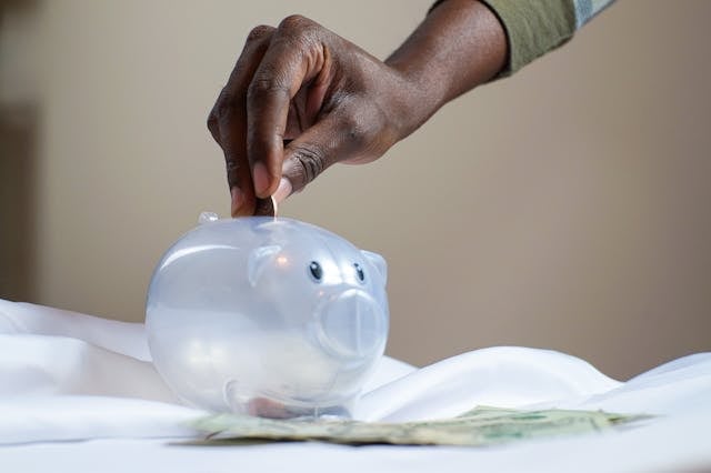 hand-placing-coin-into-transparent-piggy-bank-with-money-below