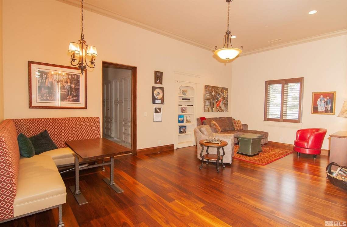 Living room with polished hardwood floors, patterned seating, built-in display shelves, and two chandeliers.