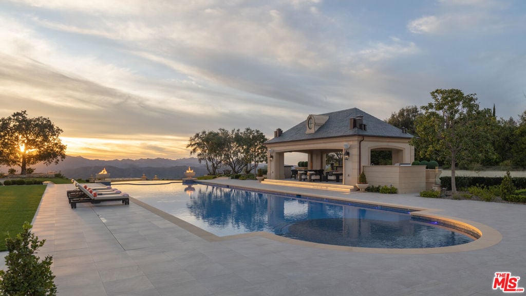 Swimming pool and covered pavilion with lounge chairs and mountain views at sunset.