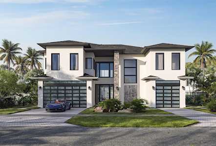Modern two-story home with twin garages, central stone entry, and palm-lined landscaping.