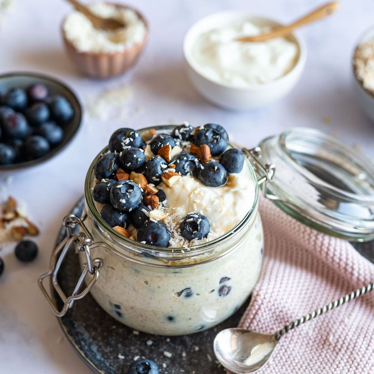 Overnight oats topped with blueberries, almonds, and coconut in a glass jar.