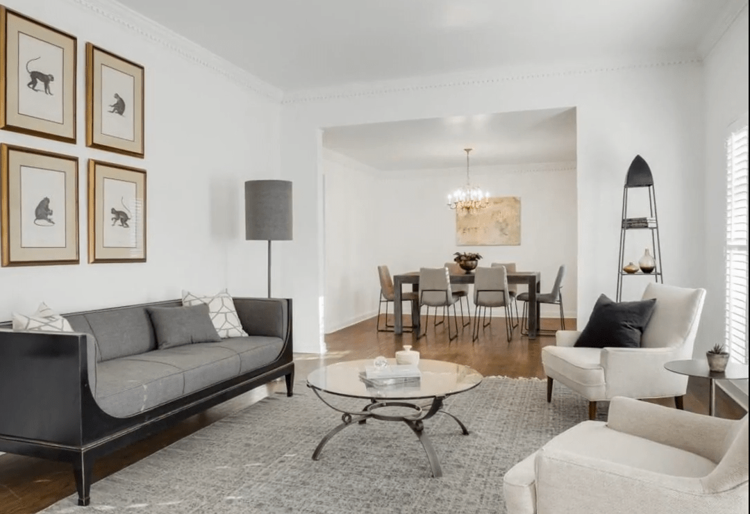 Living room with a gray sofa and white armchairs opening into a dining area.