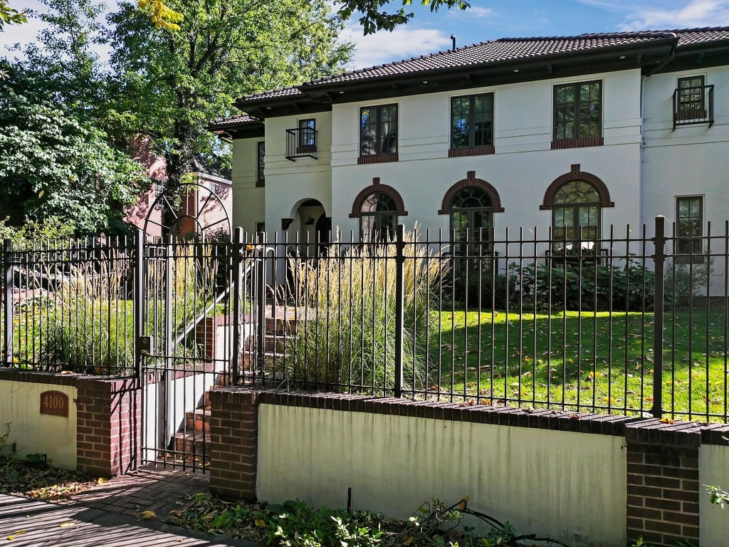 White two-story home behind an iron fence, with arched windows and a gate marked 4100.