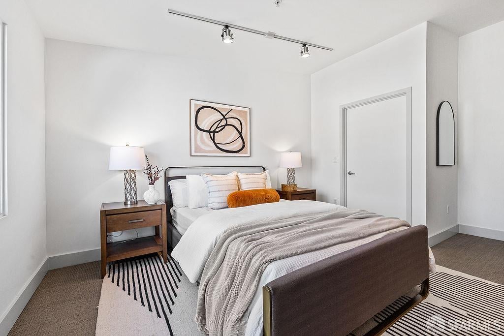 Staged bedroom with white and gray bedding, dark wood nightstands, and striped rugs.