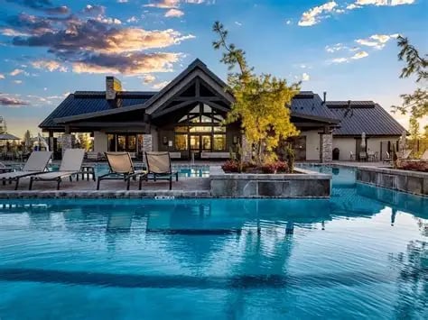Community pool beside a clubhouse with dark gabled roofs and lounge chairs.