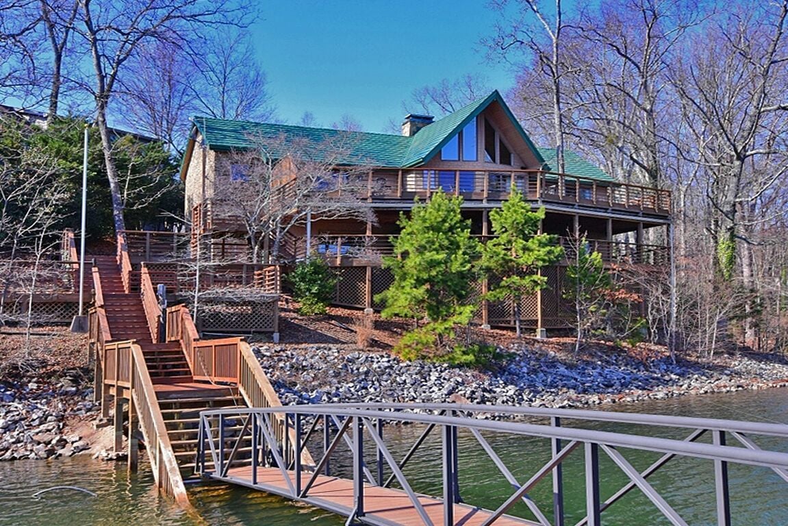 Elevated waterfront home with wraparound decks, wooded grounds, and a dock extending over the water.