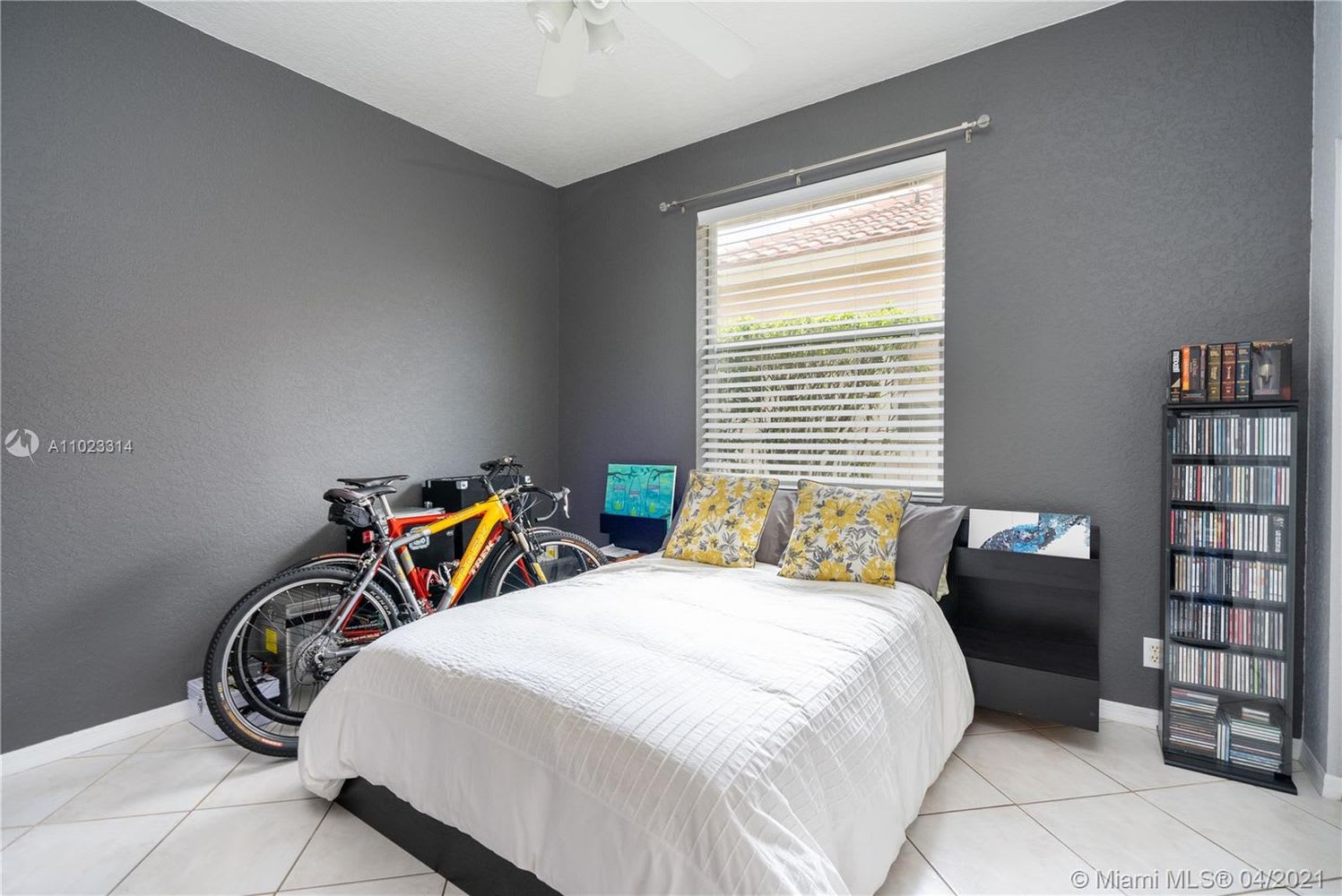 Bedroom with a white bed, dark gray walls, bicycles, and a tall CD rack.