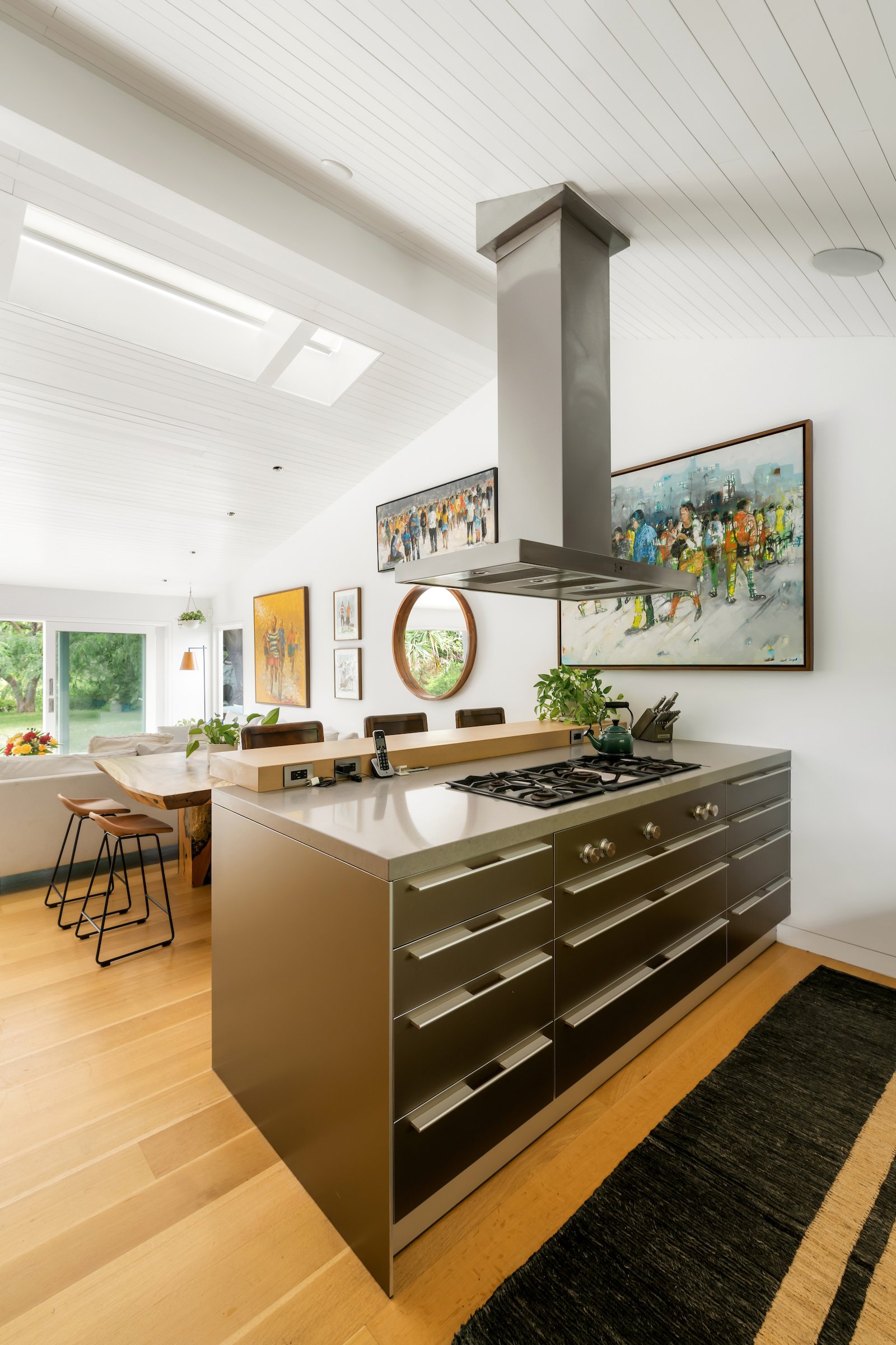 Open-plan kitchen with a stainless-steel island and suspended range hood beside a dining area and garden doors.