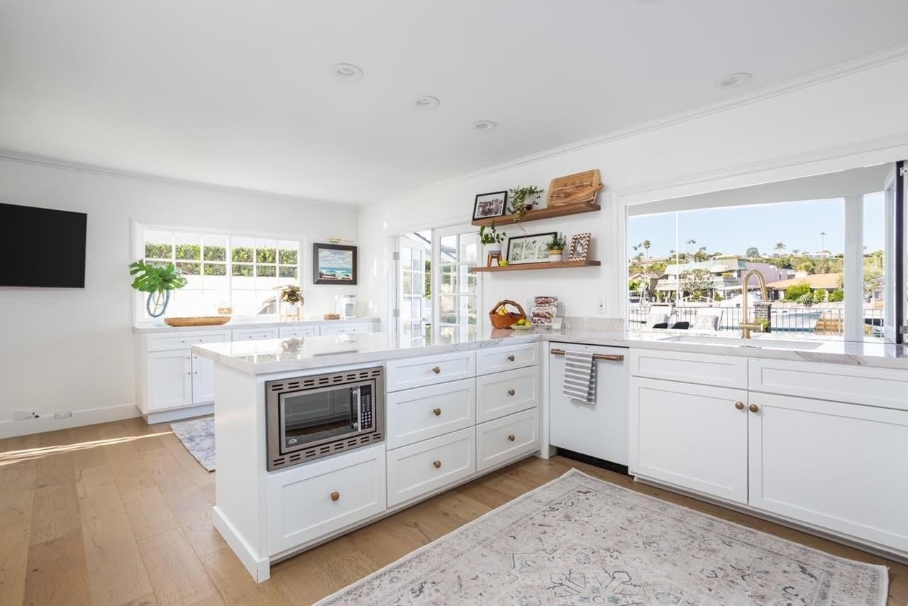  A clean and bright white kitchen with a built-in microwave, an island with drawers, and large windows with a view.