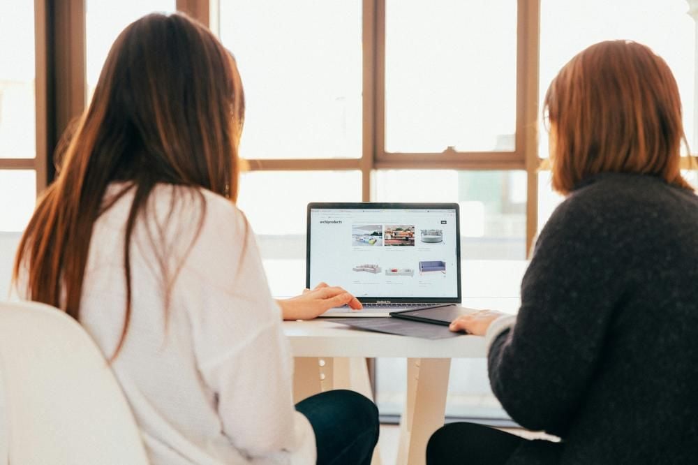 Two women look at a website together on a laptop at a table.