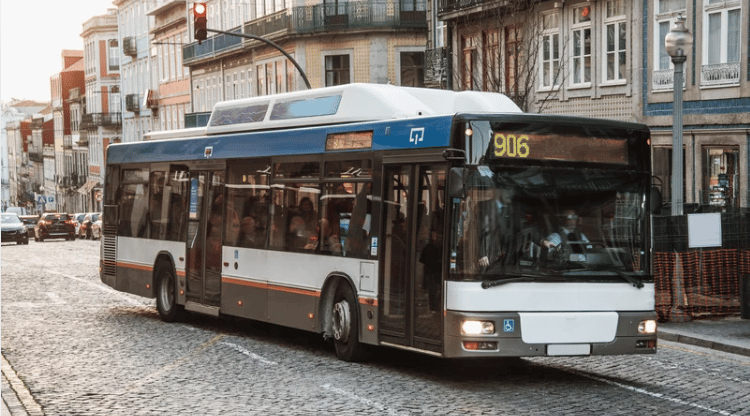 A route 906 city bus turns along a cobblestone street lined with multistory buildings.