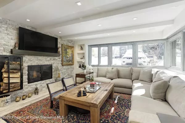 Living room with a stone fireplace, sectional sofa, and broad windows overlooking snow.