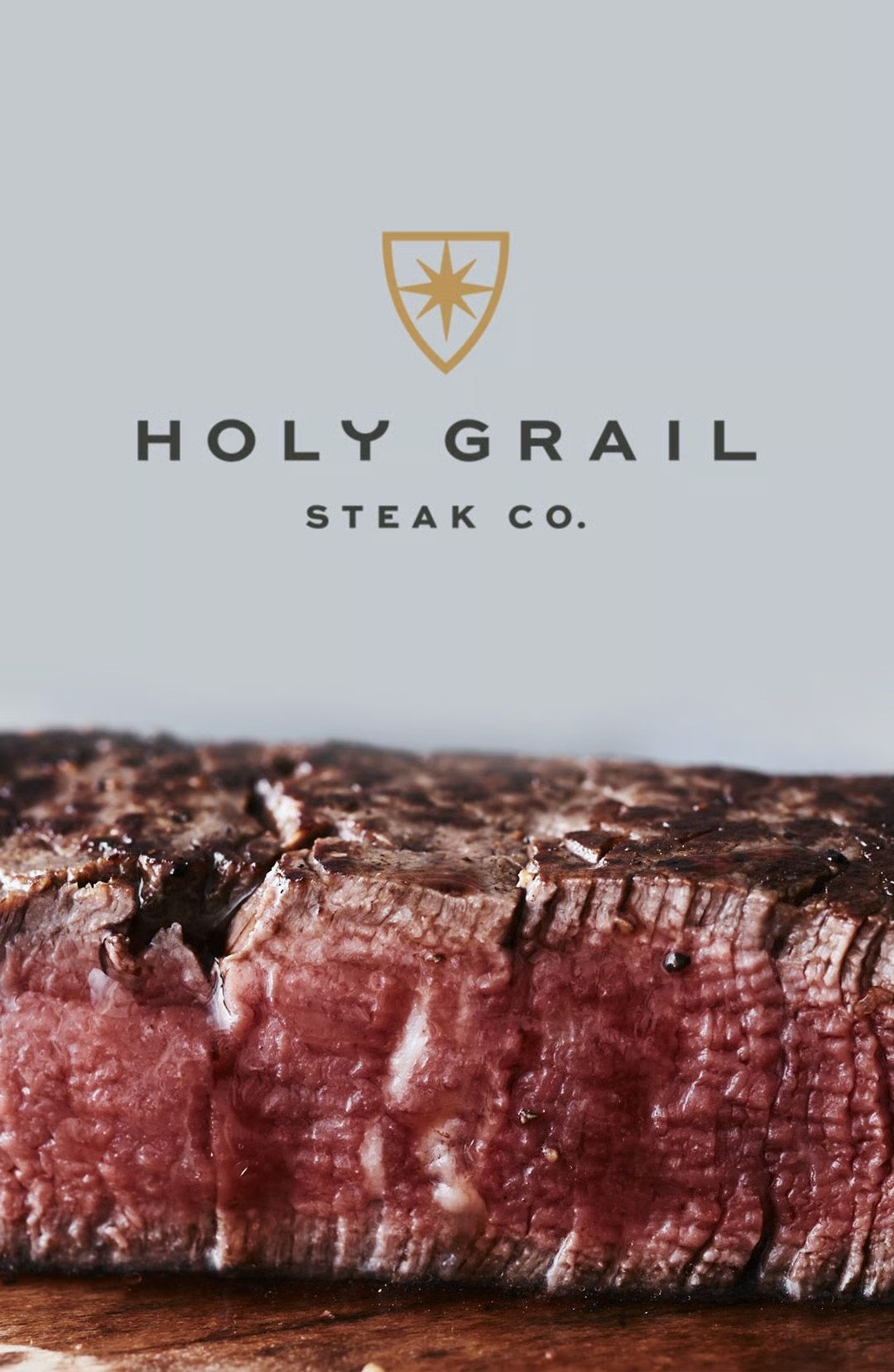 Sliced medium-rare steak on a wooden board beneath the Holy Grail Steak Co. logo.