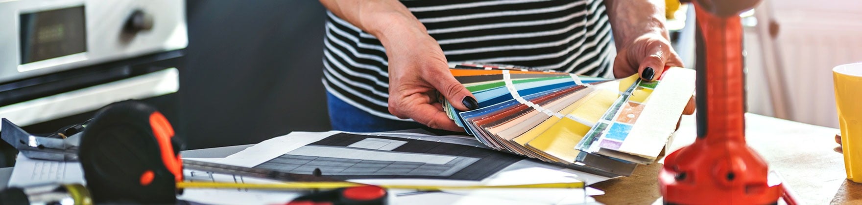 Person choosing paint colors from swatches beside renovation plans and tools.