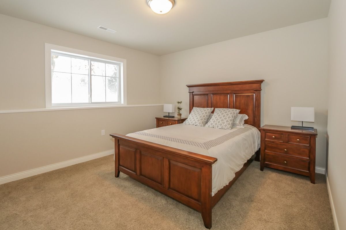 Staged bedroom with a large wooden bed, matching nightstands, and a bright window.