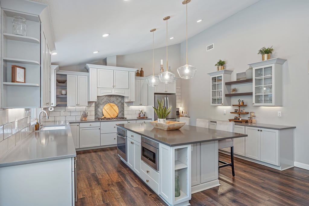 Bright kitchen with white cabinets, a large island, pendant lights, and dark wood floors.