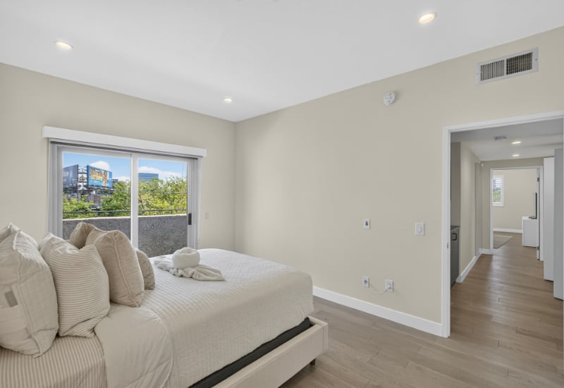 Furnished bedroom with a white bed beside a sliding glass door overlooking a balcony.
