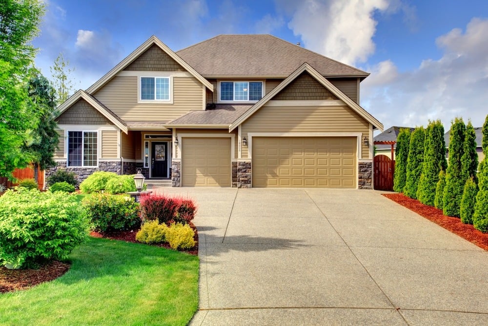 Beige two-story home with two garage doors, a broad driveway, and landscaped front yard.