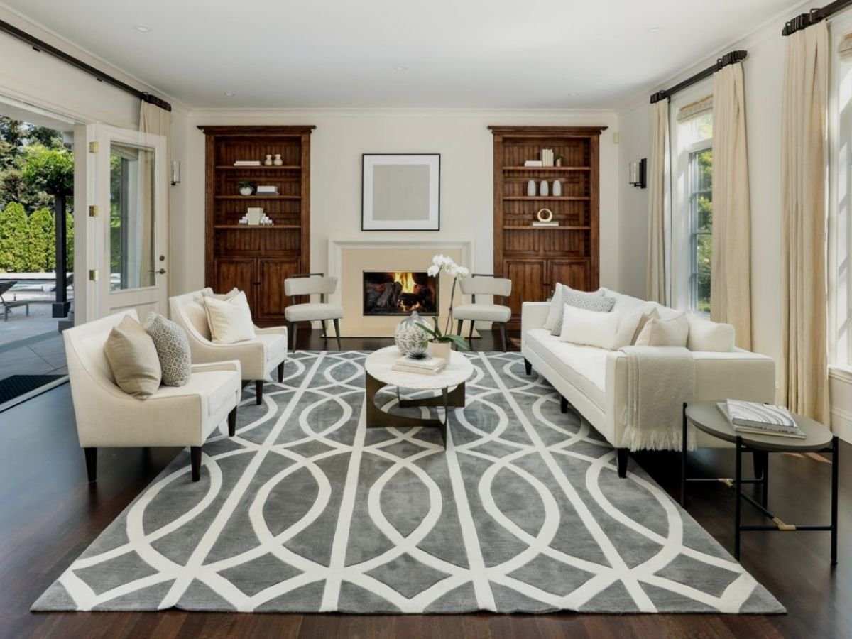 Bright, elegant living room in an Atherton home featuring a fireplace, built-in wood shelving, white seating, large windows, and French doors opening to the patio.