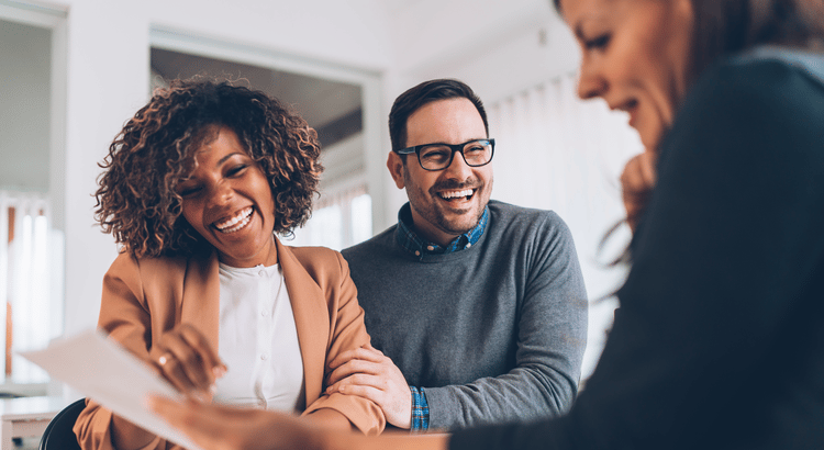 Two adults smile while reviewing a document with another person in a bright office.