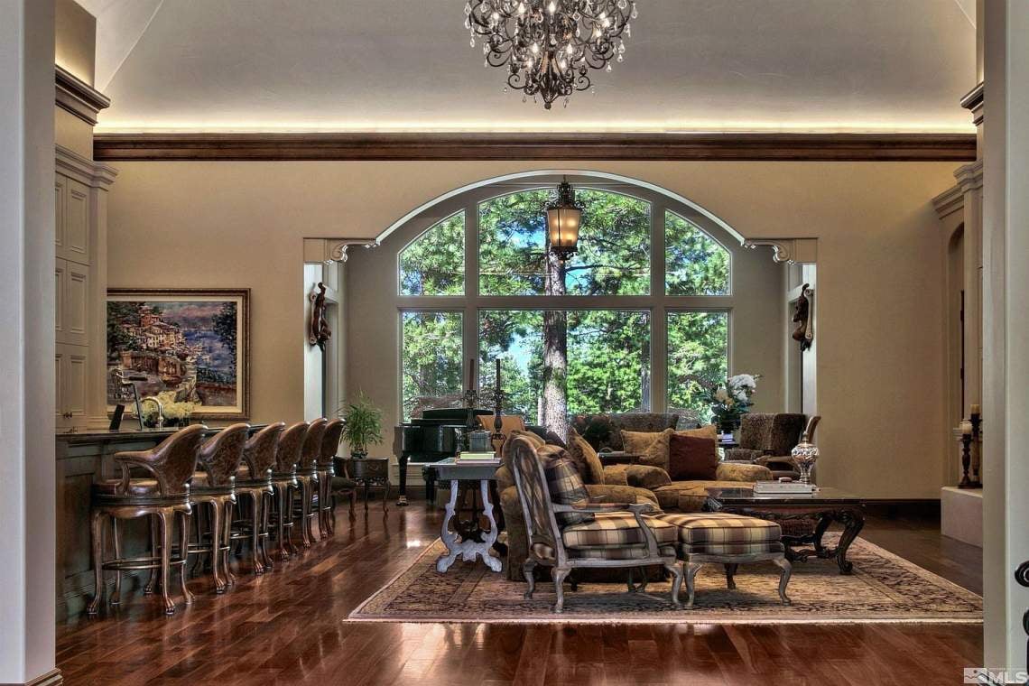 Furnished living room with an arched window overlooking trees and a grand piano.