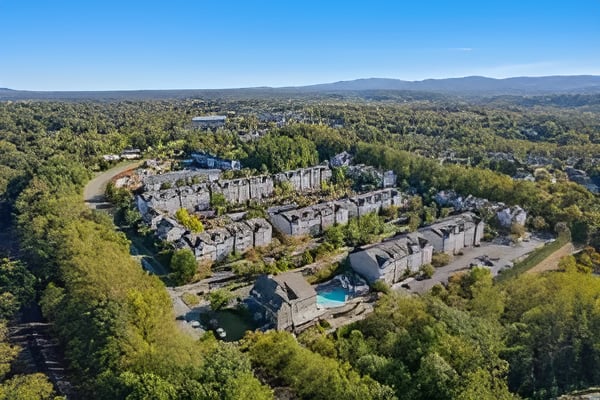 A wooded development of stone buildings with a swimming pool and distant mountain ridges.