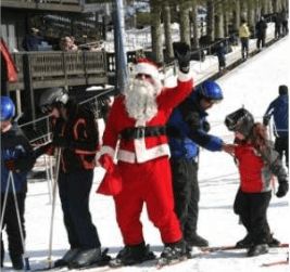 Santa Claus waves on skis beside other skiers on a snowy slope.
