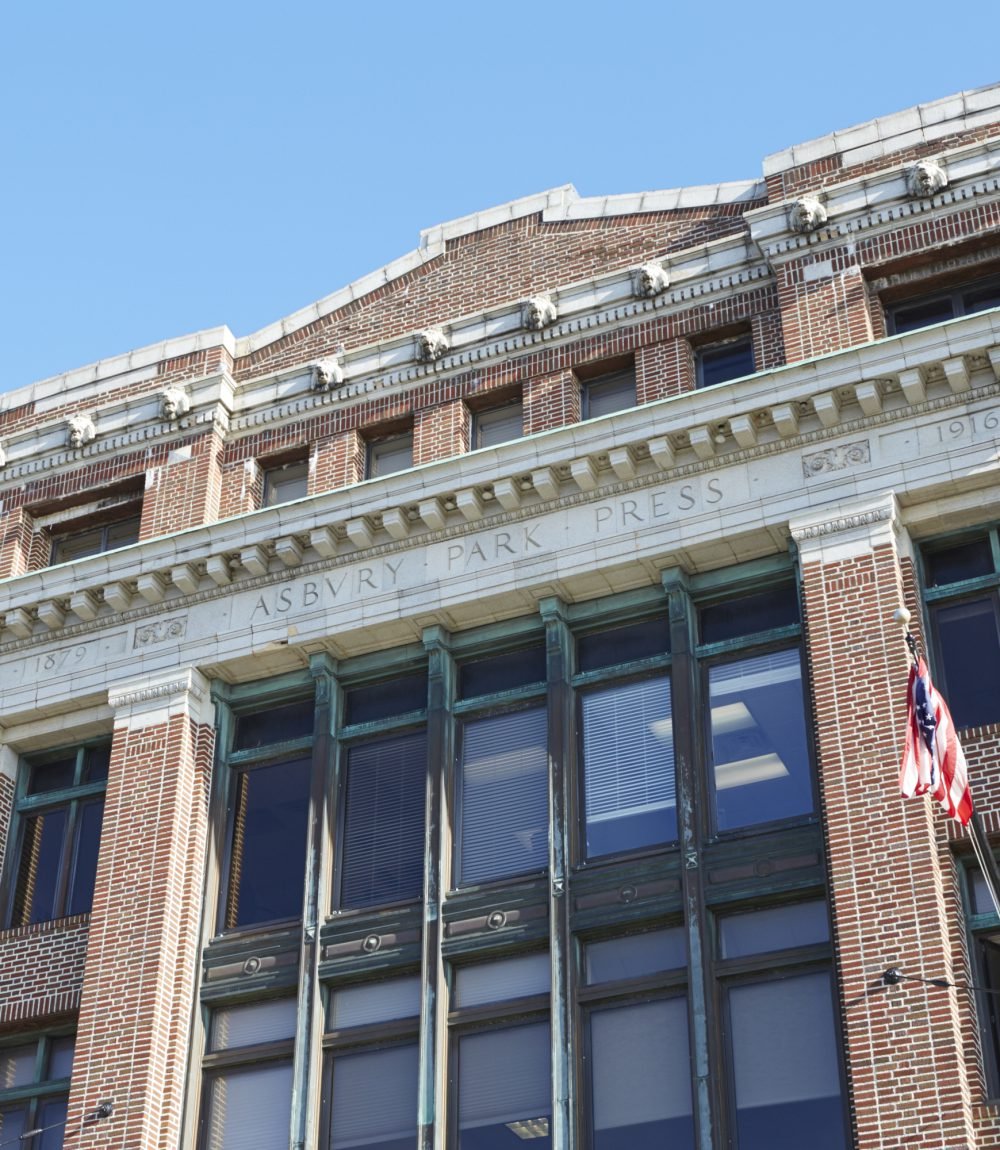 Historic Asbury Park Press building with a carved stone facade and American flag.