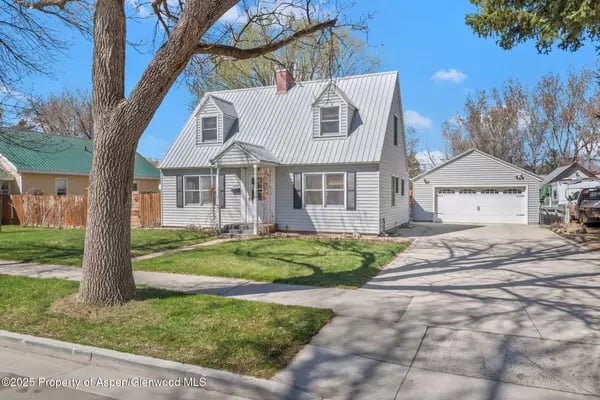 Gray house with front dormers, detached garage, and a large tree in the front yard.