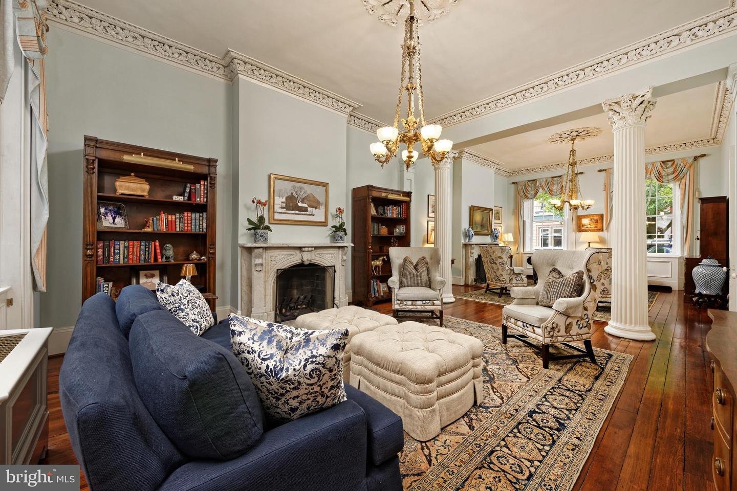 Living room with ornate molding, white columns, marble fireplace, navy sofa, and cream tufted ottomans.
