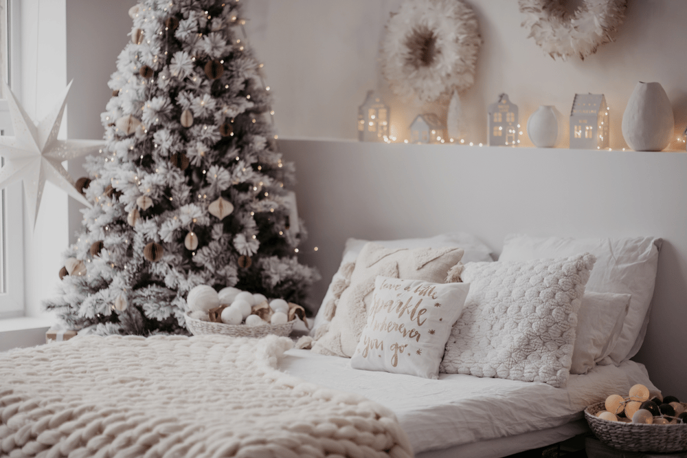 Holiday-decorated bedroom with a flocked Christmas tree and layered white knit bedding.