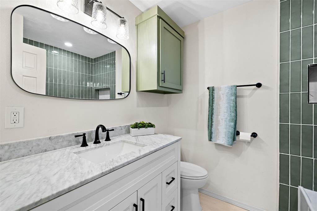 Bathroom with a marble vanity, sage-green cabinet, and dark green tile.