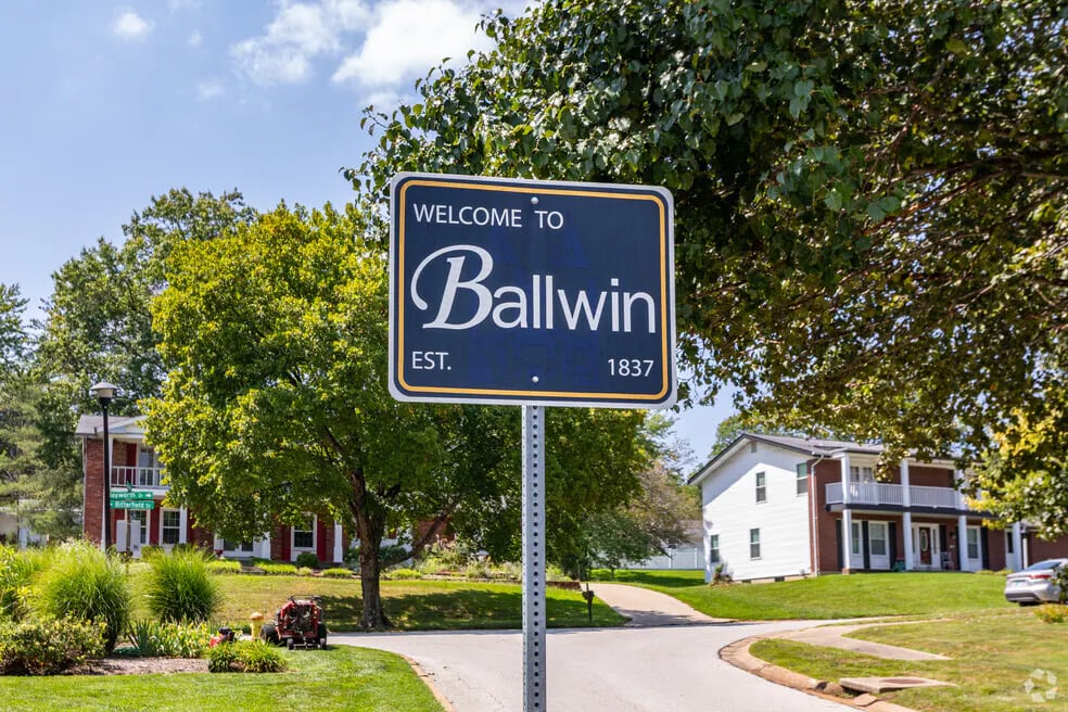 Ballwin welcome sign beside a residential street, with leafy trees and houses.