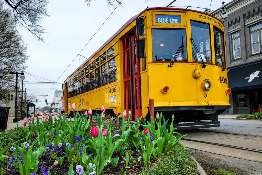 Yellow Rock Region Metro streetcar on a downtown Little Rock street beside a bed of spring flowers.