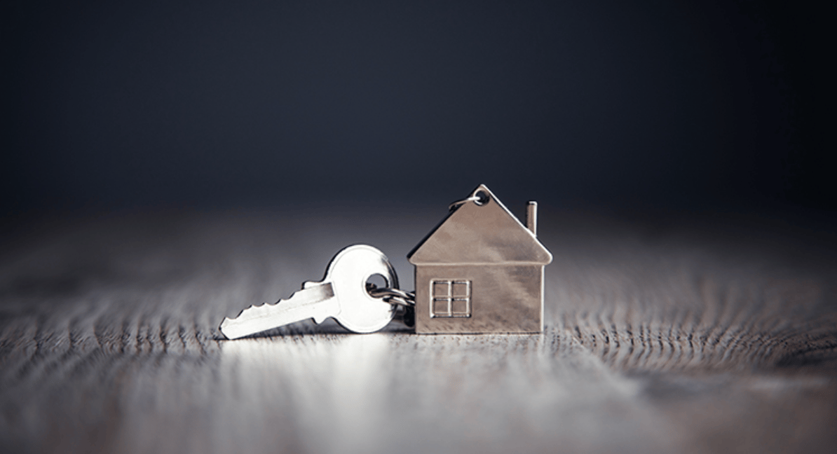 A silver house-shaped keychain attached to a key on a dark wooden surface.