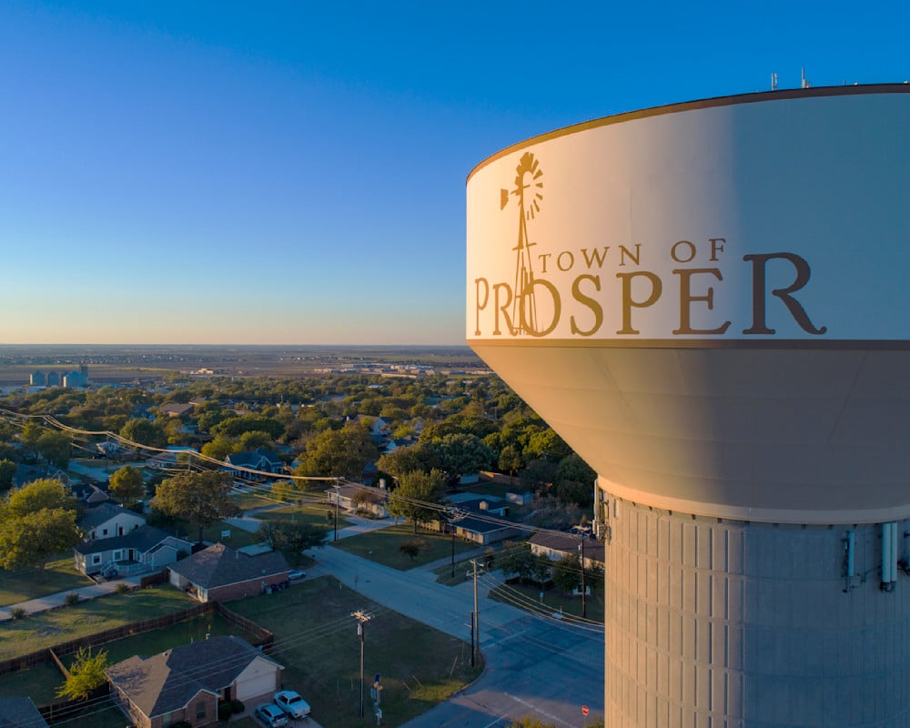 Prosper water tower overlooking homes and streets at golden hour.