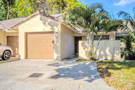 Light stucco home with a single-car garage, wide driveway, and palm trees by the entrance.