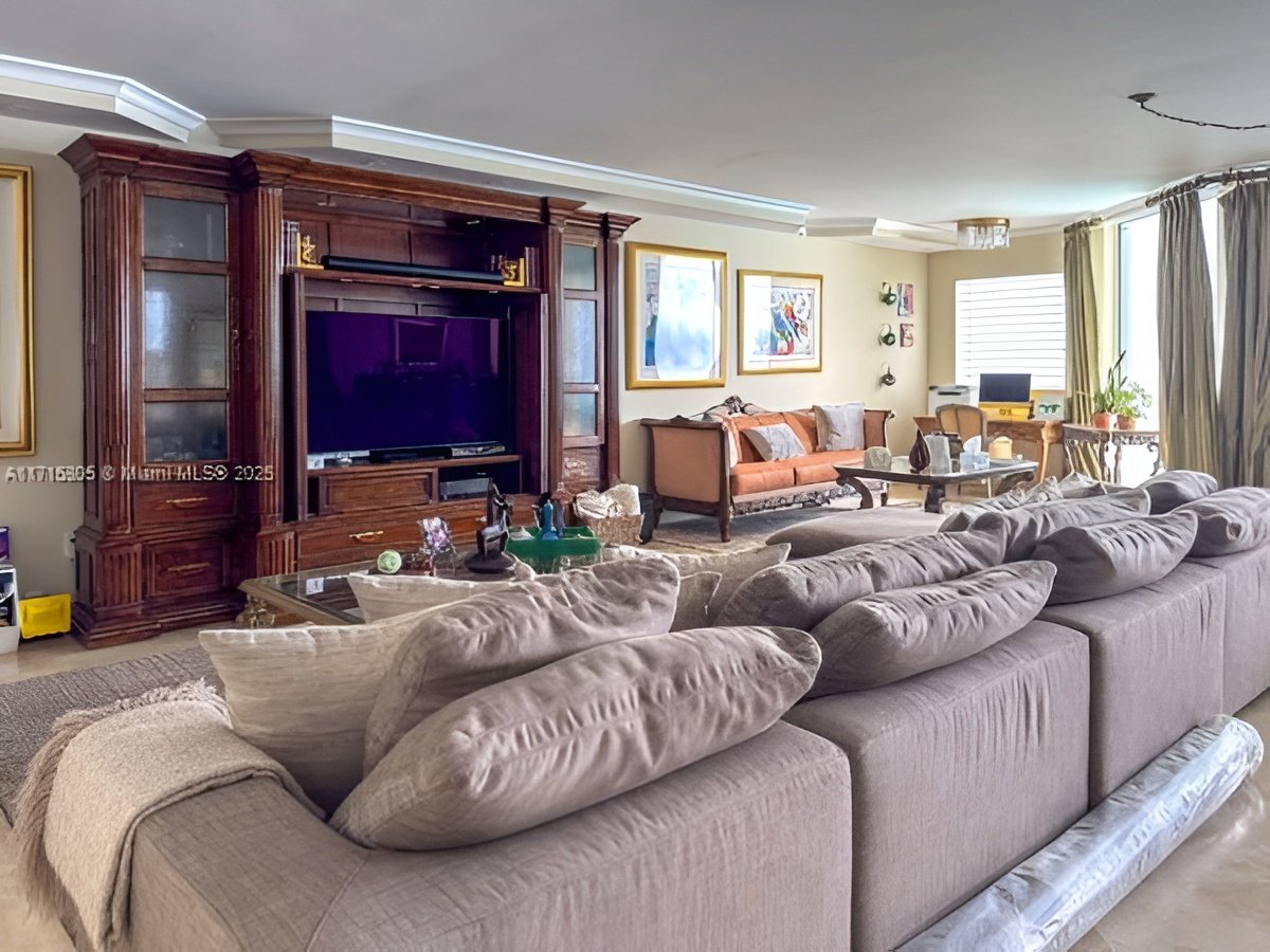 Living room with a gray sectional, glass coffee table, and ornate dark wood entertainment center.