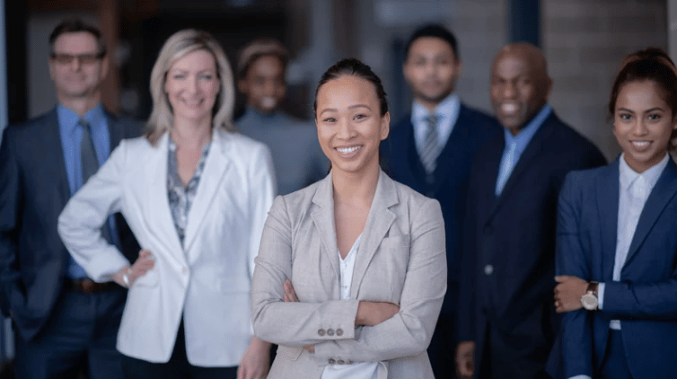 A smiling businesswoman stands with arms crossed in front of six colleagues.