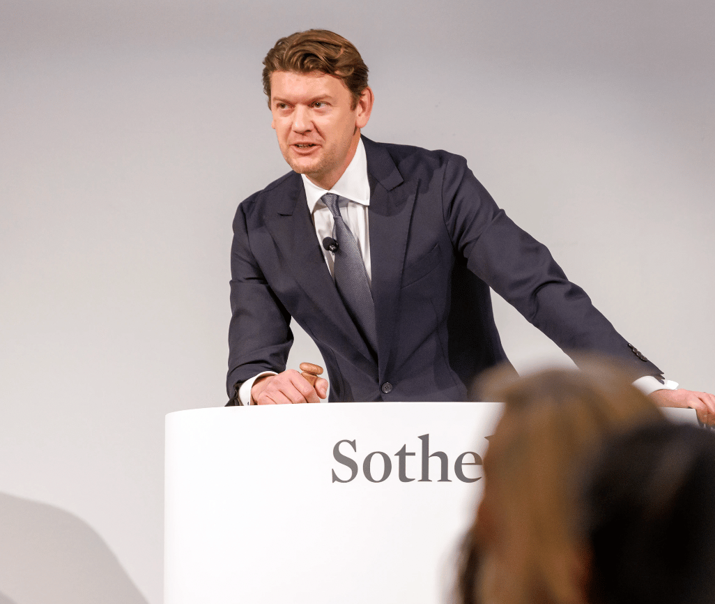 Man in a dark suit speaking at a Sotheby’s auction podium with a small gavel.