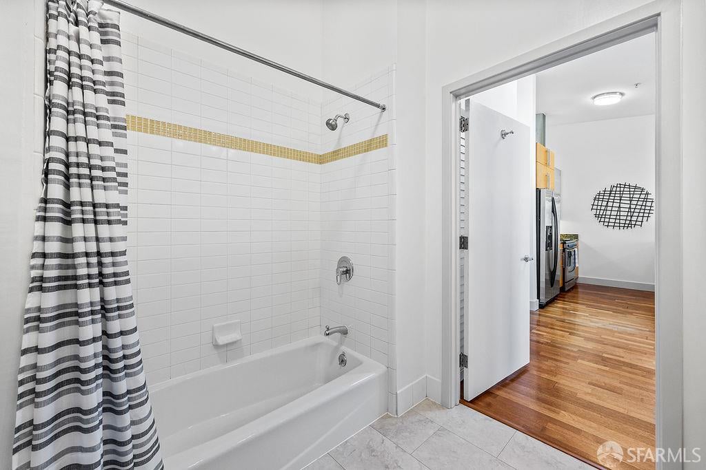 Bathroom with a tiled bathtub, striped shower curtain, and doorway to the kitchen.