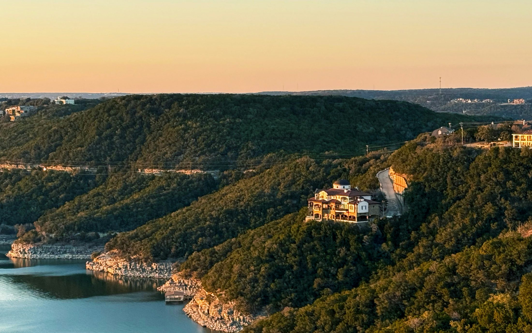 Homes and wooded limestone hills above Lake Travis at sunset.