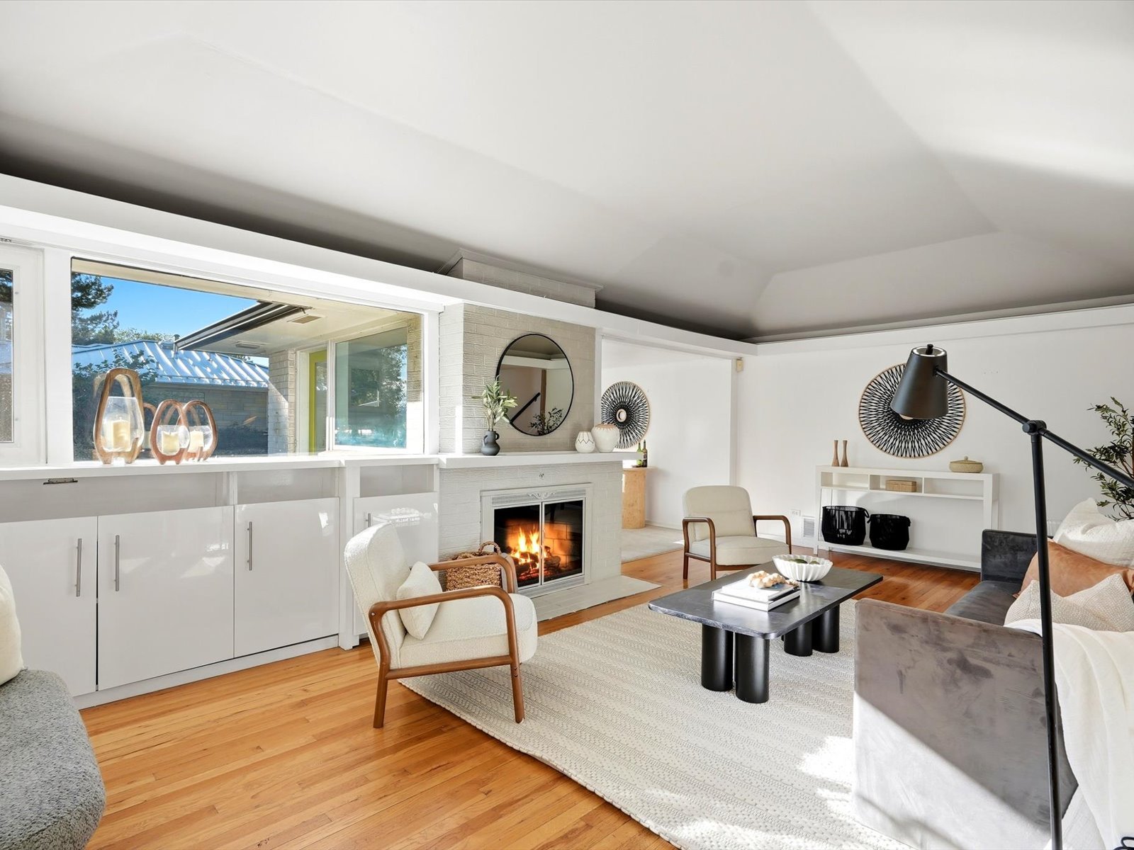 Mid-century modern living room with a white brick fireplace, wood floors, and neutral furnishings.