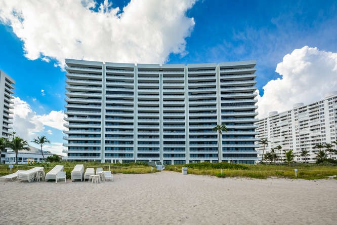 The Addison condominium tower behind a sandy beach area, with lounge chairs and neighboring high-rises.