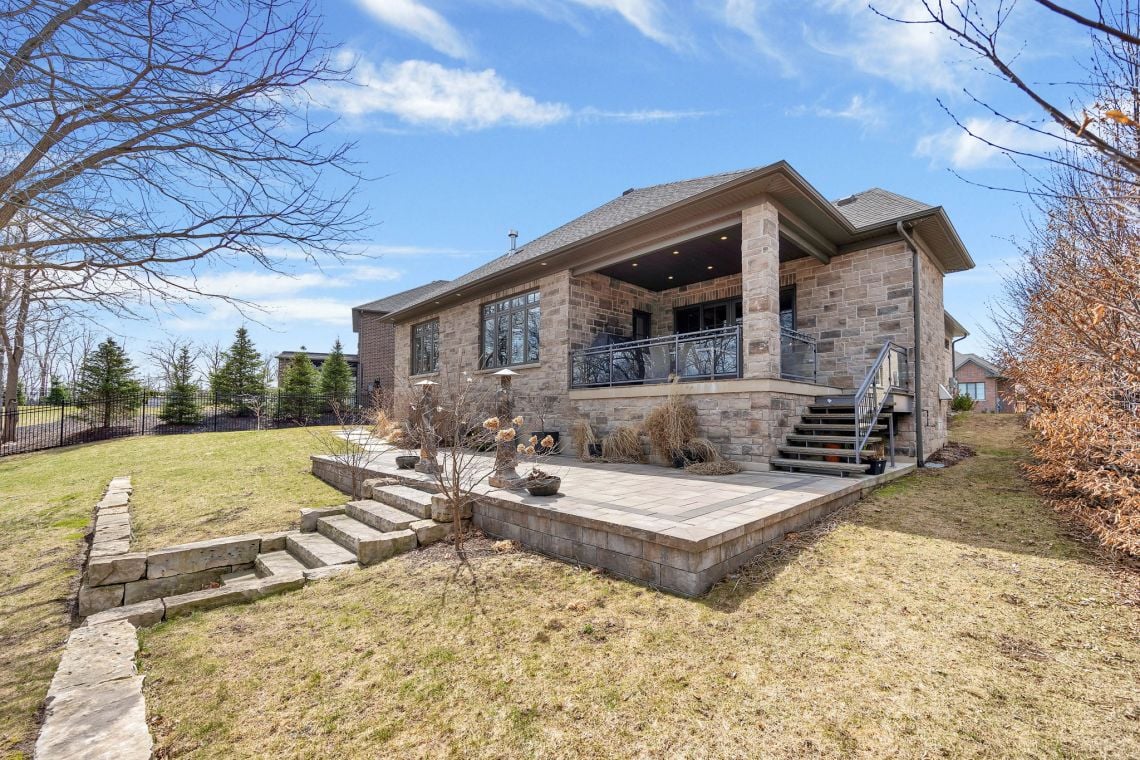 Stone house with a covered balcony and raised patio overlooking a lawn.