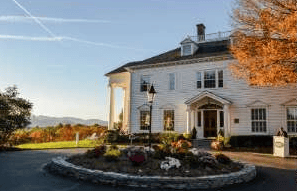 White two-story house with a columned entrance, curved driveway, and autumn foliage.